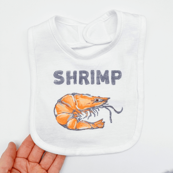 A hand holding a bib with an orange shrimp on it.