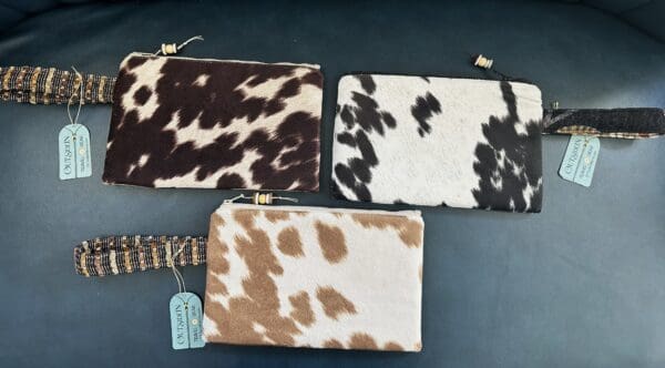 Three cowhide zippered pouches with tags.