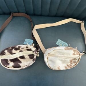 Two cow print fanny packs with straps.