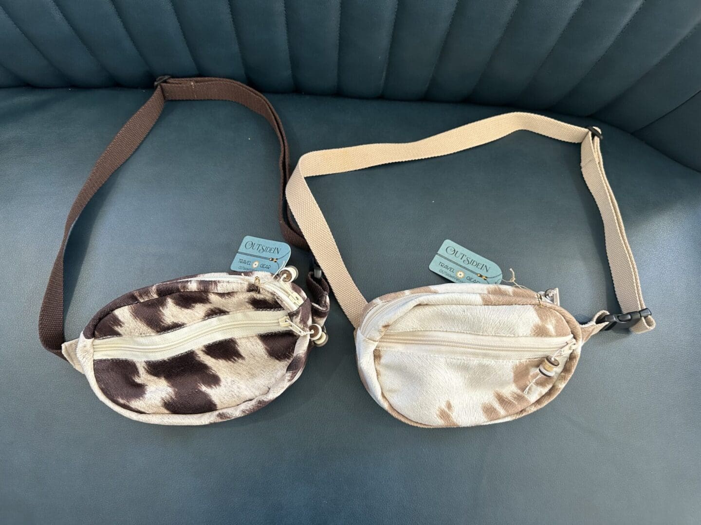 Two cow print fanny packs with straps.