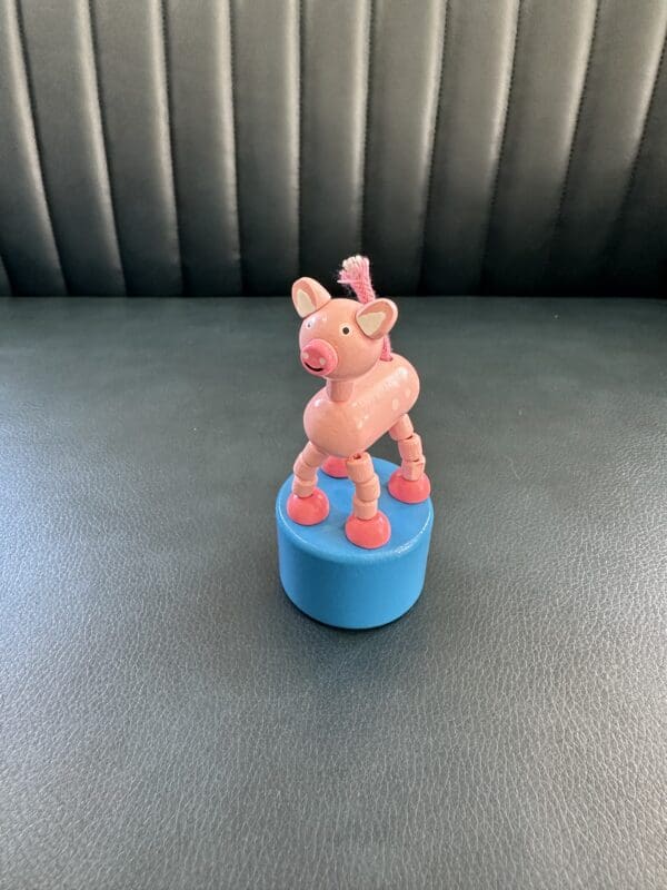 Pink wooden pig toy on blue base.