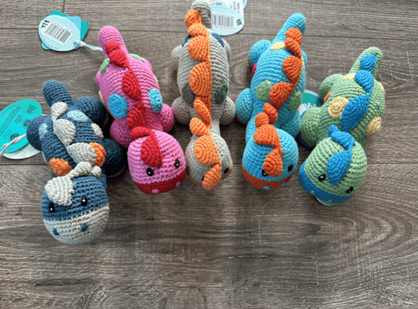 Five colorful crocheted dinosaur toys.